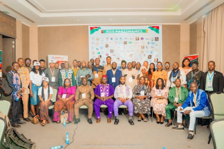 Photo de groupe des participants aux Rencontres Networking des Formateurs du Burkina Faso, devant le panneau des partenaires
